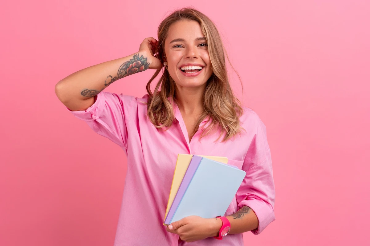 Mujer joven sonriendo y sosteniendo cuadernos, representando cercanía y atención personalizada.